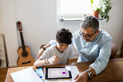 Father assisting son in using digital tablet while studying at home