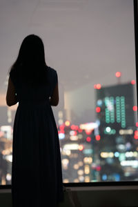 Rear view of woman standing against window in city