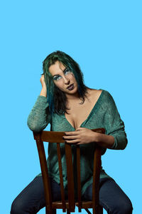 Young woman sitting on chair against blue background