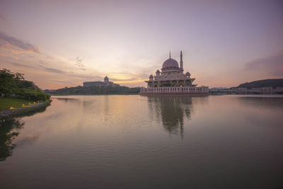 Mosque by lake against sky during sunset