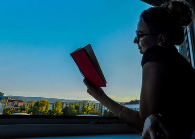 Side view of young woman using smart phone against sky