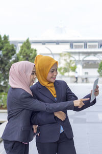 Happy businesswomen taking selfie through digital tablet while standing on street