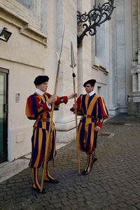 Rear view of men standing on footpath against building