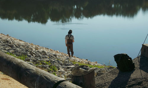 Rear view of man fishing on lake against sky