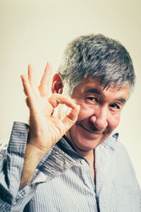 Portrait of senior man gesturing ok sign while standing against beige background