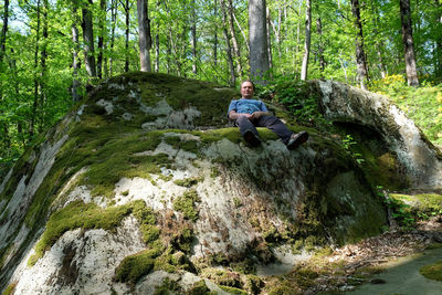 Portrait of man sitting on rock at forest