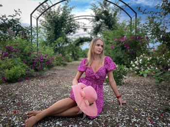 Woman wearing pink summer dress and hat resting on the ground in a garden full of colorful roses