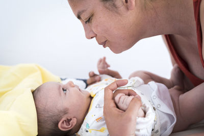 Affectionate mother looking at baby while holding his hands