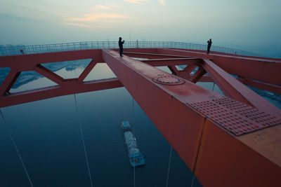 Men standing on railing over river against sky