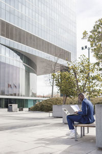 Businessman holding document using laptop sitting on bench