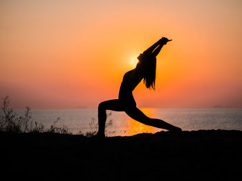 Side view of woman doing exercising on field against sea during sunset