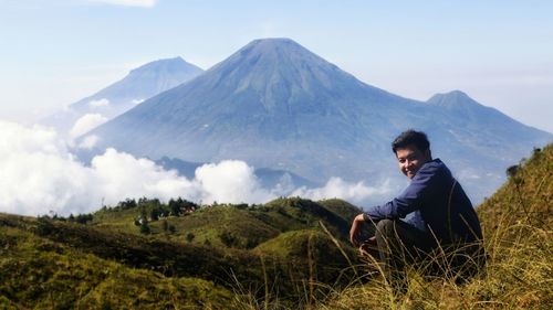 Portrait of smiling young man sitting on grass against mountains