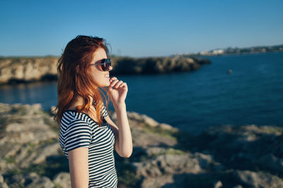 Young woman wearing sunglasses standing by sea