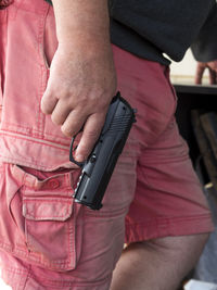 Midsection of man holding gun behind back