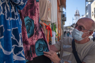 Close-up of senior man wearing mask looking at garment for sale at market