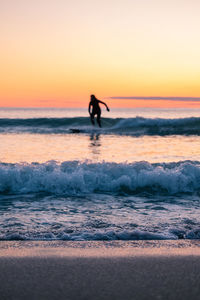 Silhouette woman surfing on sea against clear sky during sunset