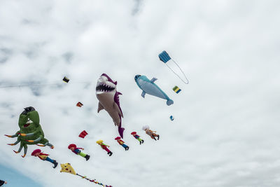 Low angle view of various colorful balloons flying against cloudy sky