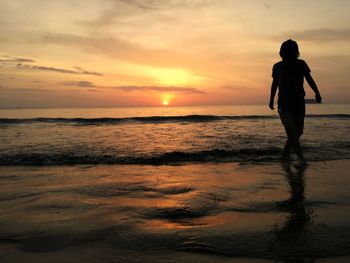 Silhouette woman walking at beach against sky during sunset