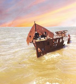 Abandoned boat on beach against sky during sunset