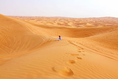 Young woman sitting on sand dune against clear sky