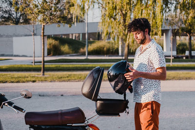 Young handsome male with hipster outfit takes the helmet out from the basket or trunk.