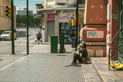 Man sitting on footpath in city