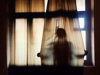 Rear view of woman standing by window at home