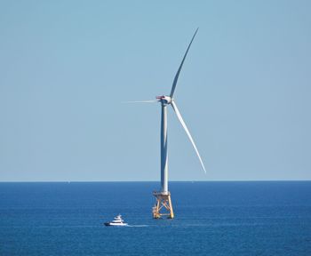 Boat under windmill at sea under clear sky