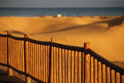 Fence on beach against sky during sunset