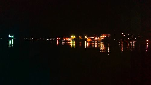 Illuminated city by lake against sky at night