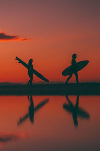 Silhouette men standing against orange sky during sunset