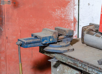 Old blue iron vise on workbench workshop in blurred environment of other equipment and tools,
