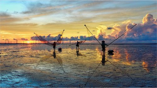 Silhouette people on beach against sky during sunset