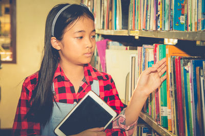 Girl selecting book with digital tablet in library