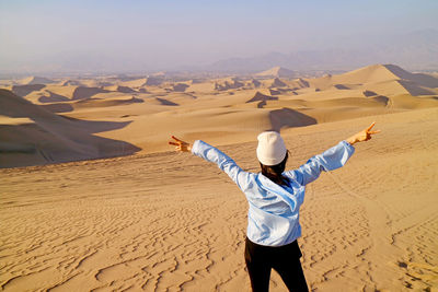 Joyful female traveler raising arms on the sand dune of huacachina desert, ica province, peru