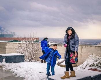Family playing with snow while standing on building terrace against cloudy sky