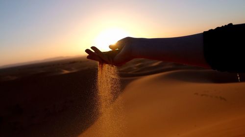 Close-up of hand on sand at beach against sky during sunset