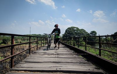 Rear view of man walking on footbridge against sky