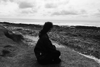 Woman sitting on beach against sky