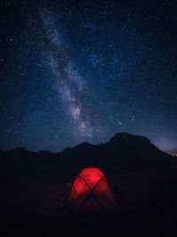 Illuminated tent on mountains against star field in sky at night