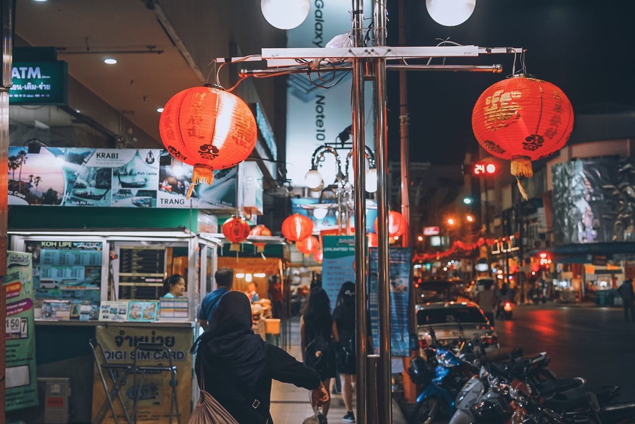 illuminated, lighting equipment, lantern, night, real people, market, built structure, women, retail, architecture, communication, city, text, lifestyles, adult, incidental people, building exterior, for sale, people, hanging, outdoors, chinese lantern, paper lantern, retail display