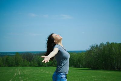 Side view of smiling young woman standing on grass against sky