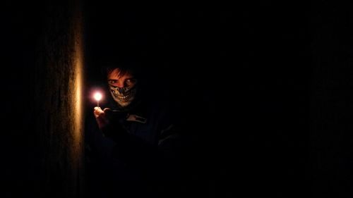 Portrait of man wearing handkerchief on face while holding burning matchstick in darkroom