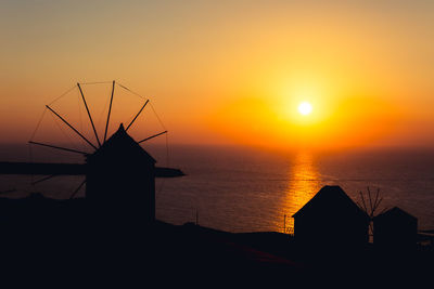 Silhouette traditional windmill by sea against sky during sunset