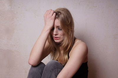 Crying young woman sitting against wall