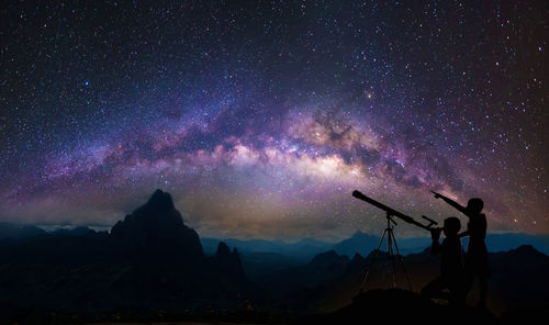 Silhouette people on mountain against sky at night