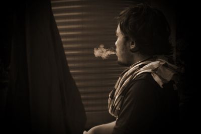 Side view of man smoking cigarette while standing in darkroom