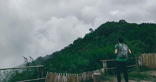 Rear view of man standing by railing against sky