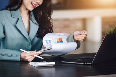 Midsection of woman using laptop while sitting on table