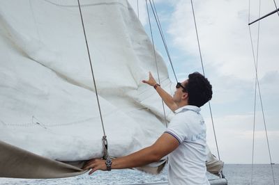 Side view of young man looking at camera against sky